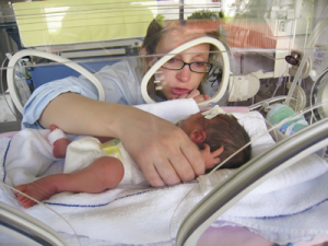 Mom touching premature baby in incubator